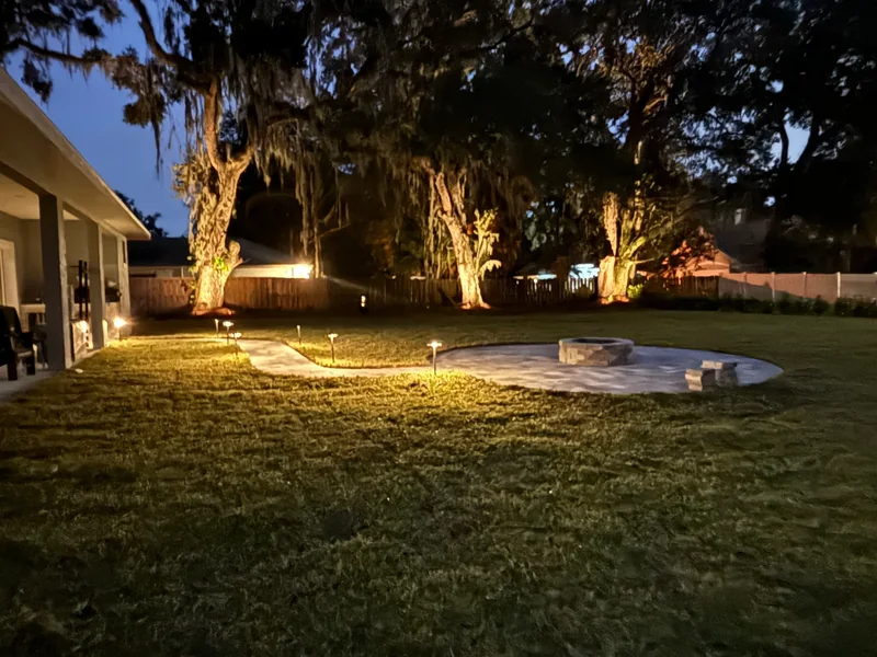 Nighttime view of custom paver walkway, fire pit, and landscape lighting in DeLand, FL backyard