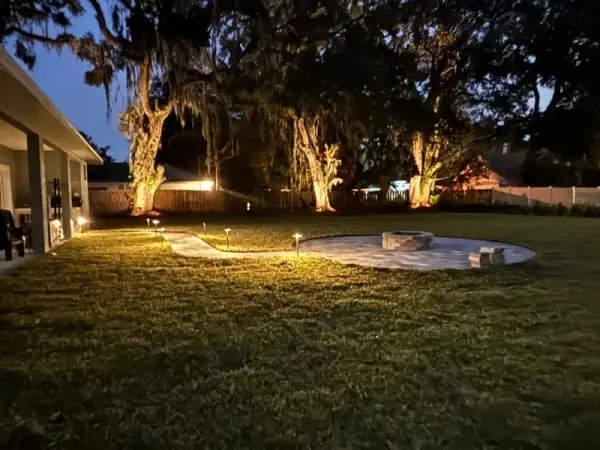 Nighttime view of custom paver walkway, fire pit, and landscape lighting in DeLand, FL backyard