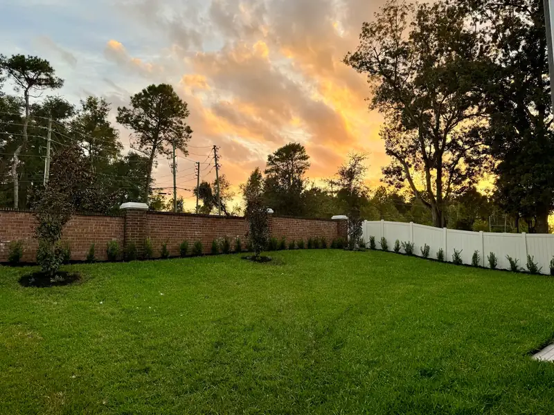 Lush green front yard landscape design in Daytona Beach with a brick wall and new plants
