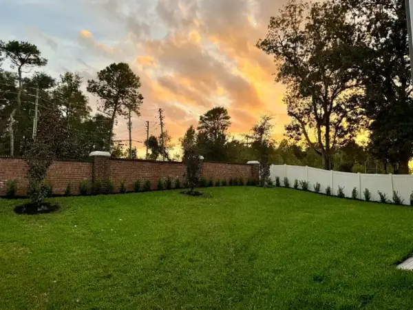 Lush green front yard landscape design in Daytona Beach with a brick wall and new plants